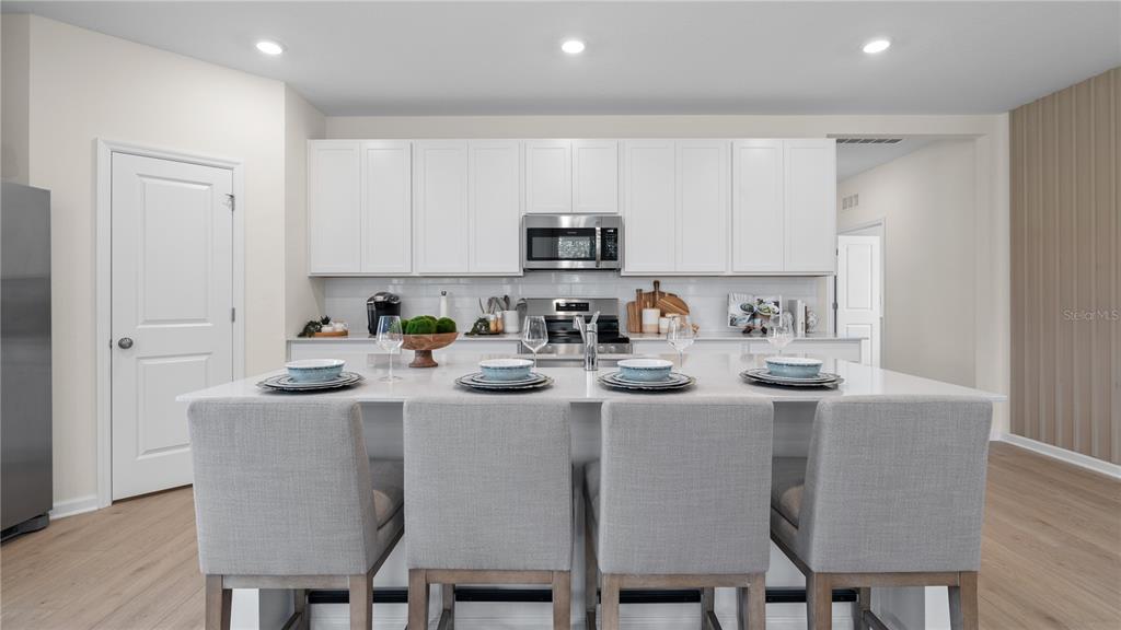 A modern kitchen features white cabinetry, a large quartz island with four chairs, and stainless appliances — 633 RUTH AVENUE, HAINES CITY, FL