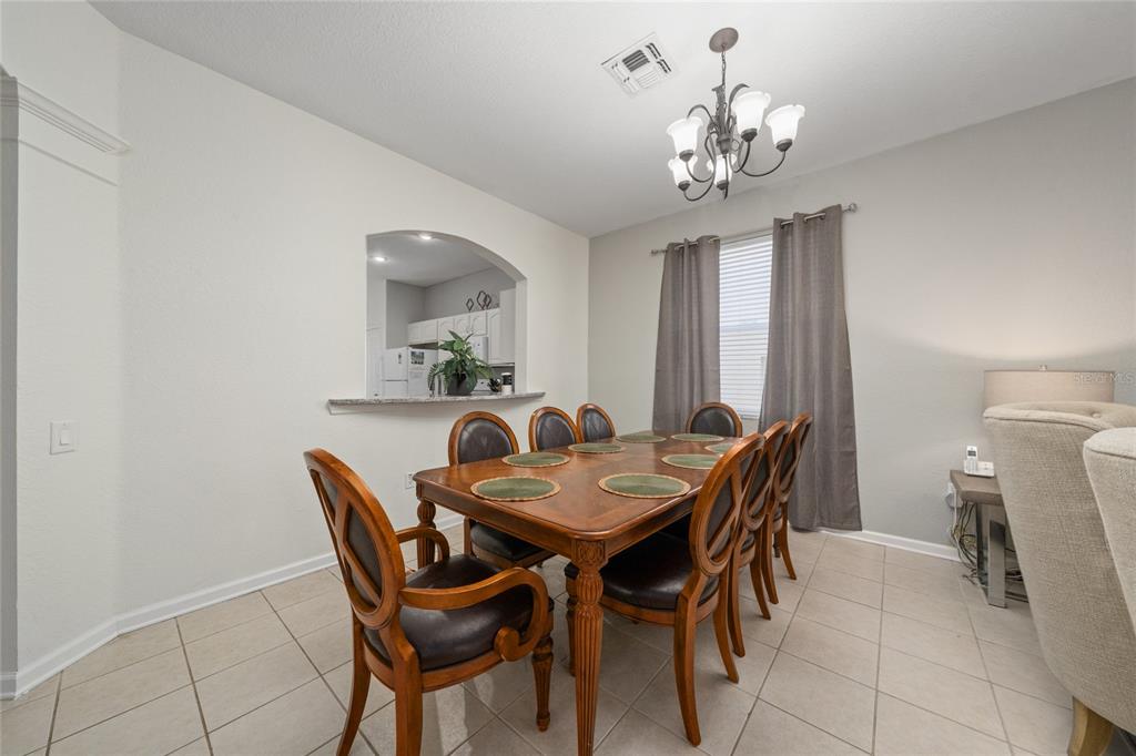 A dining room with a wooden table, six chairs, a chandelier, and a kitchen pass-through — 7765 TOSTETH STREET, KISSIMMEE, FL