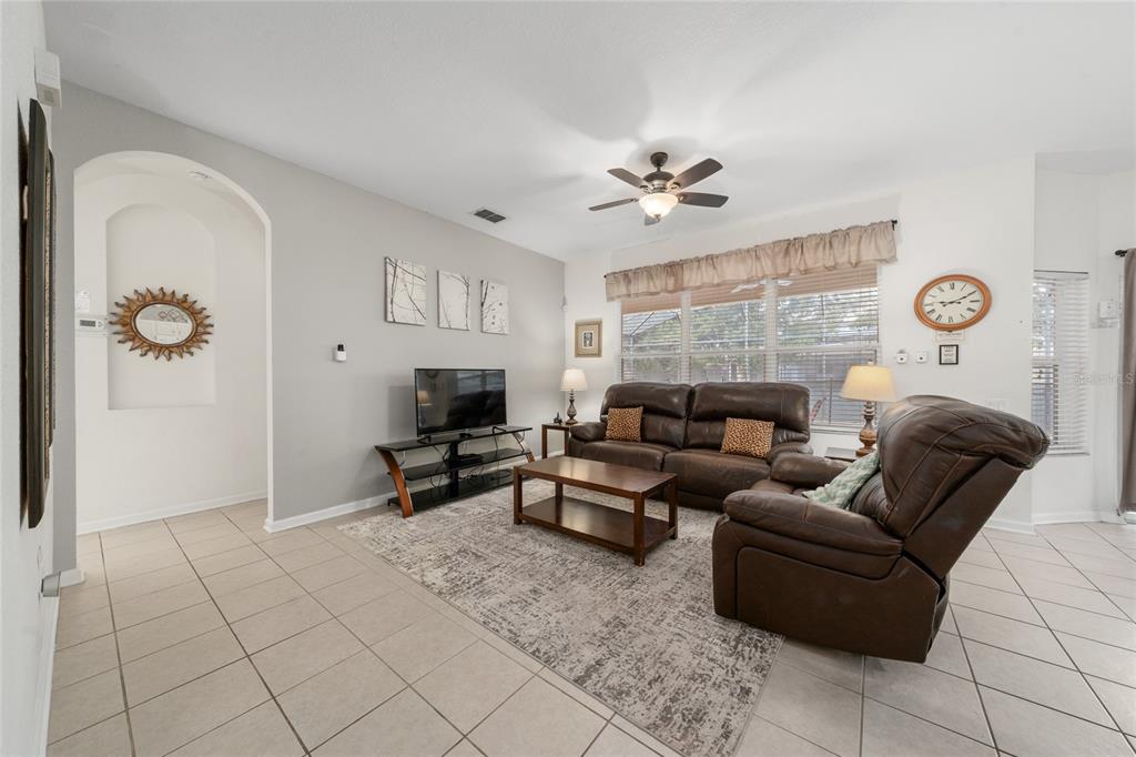 A living room features tile flooring, a brown leather sofa and recliner, and a television — 7765 TOSTETH STREET, KISSIMMEE, FL