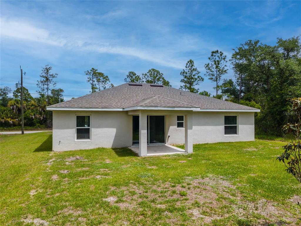 The rear exterior of a single-story house features a covered patio and a grassy yard — 1326 GLENAN ROAD, NORTH PORT, FL