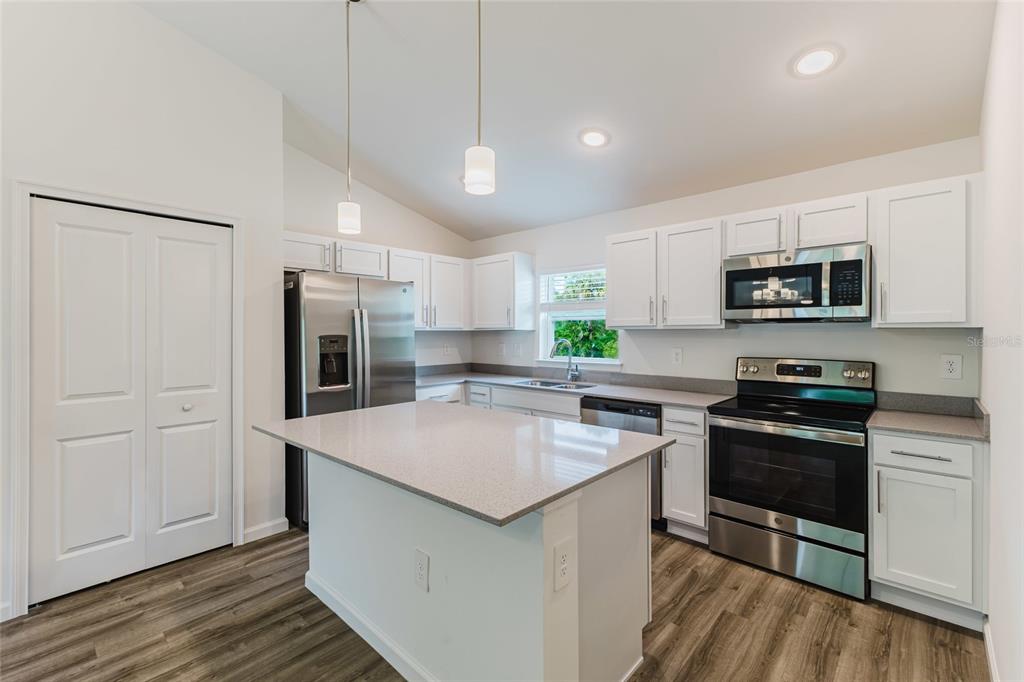 A kitchen with white cabinets, stainless steel appliances, a center island, and wood-look flooring — 1326 GLENAN ROAD, NORTH PORT, FL