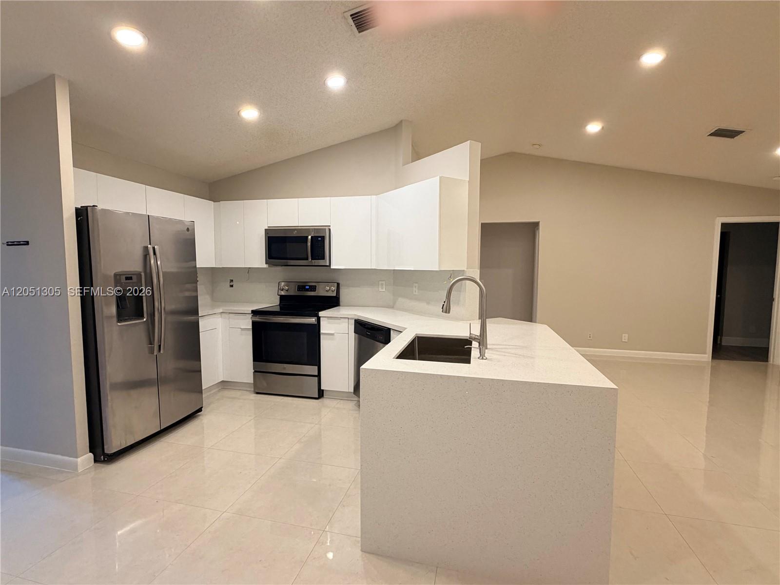 A modern kitchen features white cabinets, stainless steel appliances, and a quartz-topped island — 1547 Zenith Way, Weston FL 33327, WESTON, FL