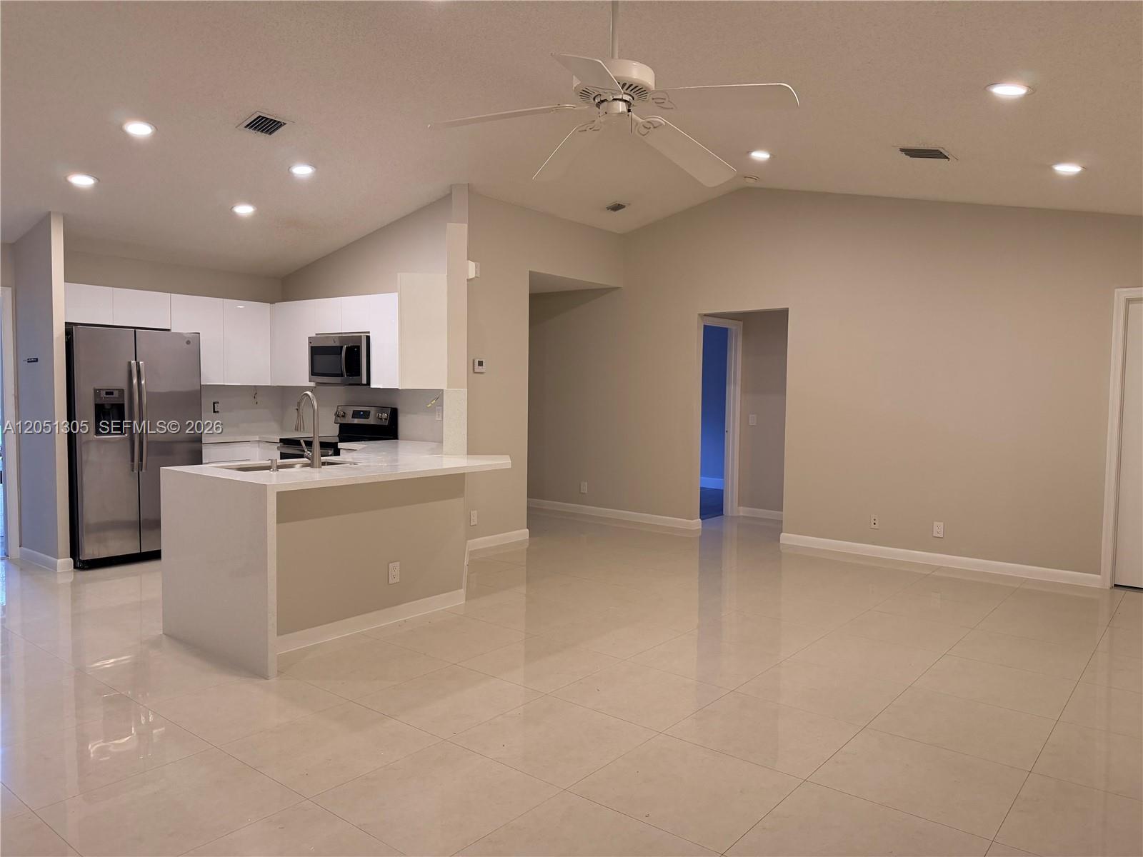 A modern kitchen with white cabinets and a peninsula overlooks an open living area — 1547 Zenith Way, Weston FL 33327, WESTON, FL