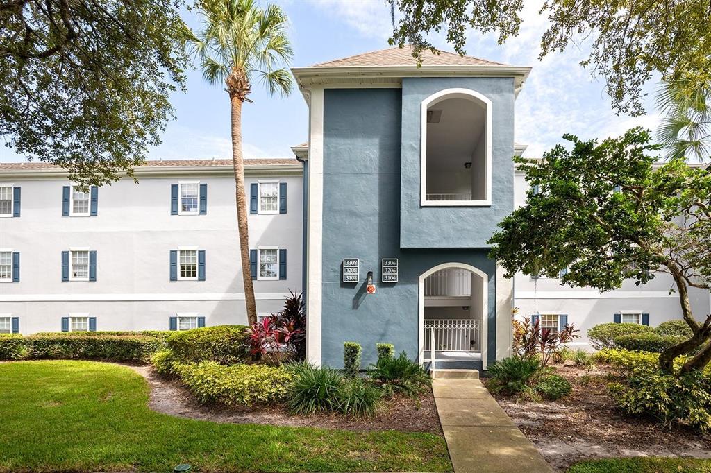 A blue and white multi-story apartment building exterior features a central entryway and landscaping — 3206 CLUBSIDE DRIVE UNIT 3206, LONGWOOD, FL