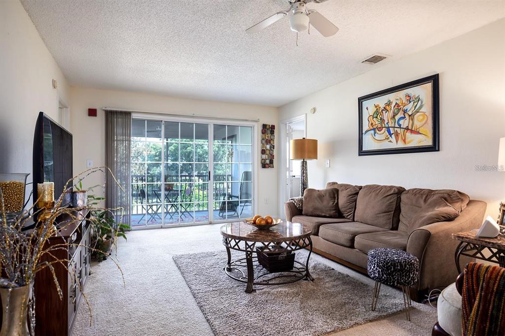 A living room features a brown sofa, a round coffee table, and sliding glass balcony doors — 3206 CLUBSIDE DRIVE UNIT 3206, LONGWOOD, FL