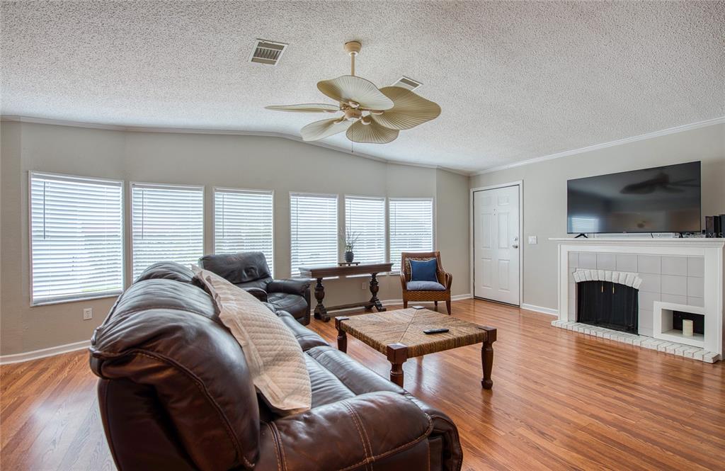 A living room features a leather sofa, a fireplace, hardwood floors, and a ceiling fan — 480 TROUT LANE, OLDSMAR, FL