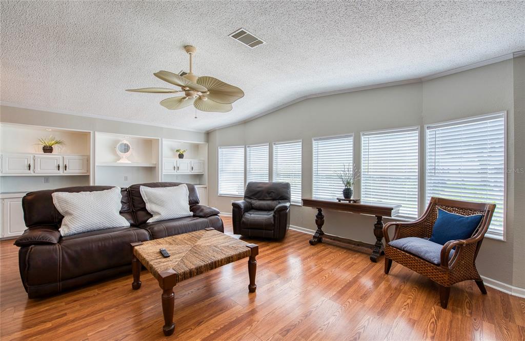 A living room features hardwood floors, a ceiling fan, built-in shelving, and several windows — 480 TROUT LANE, OLDSMAR, FL
