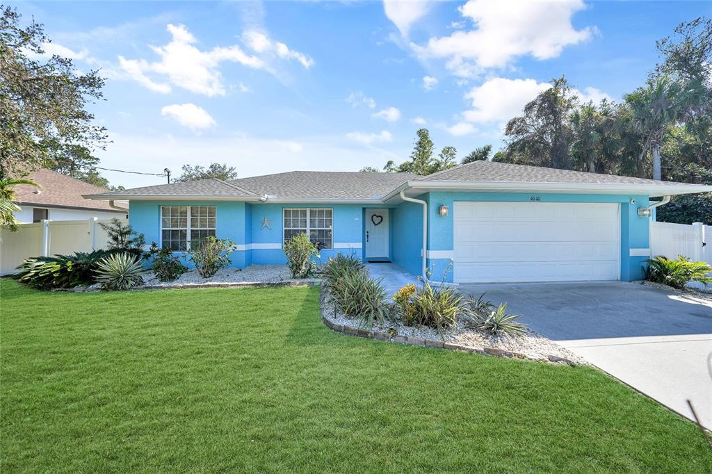 A bright blue single-story house features a white garage door and a landscaped front yard — 4040 S CRANBERRY BOULEVARD, NORTH PORT, FL