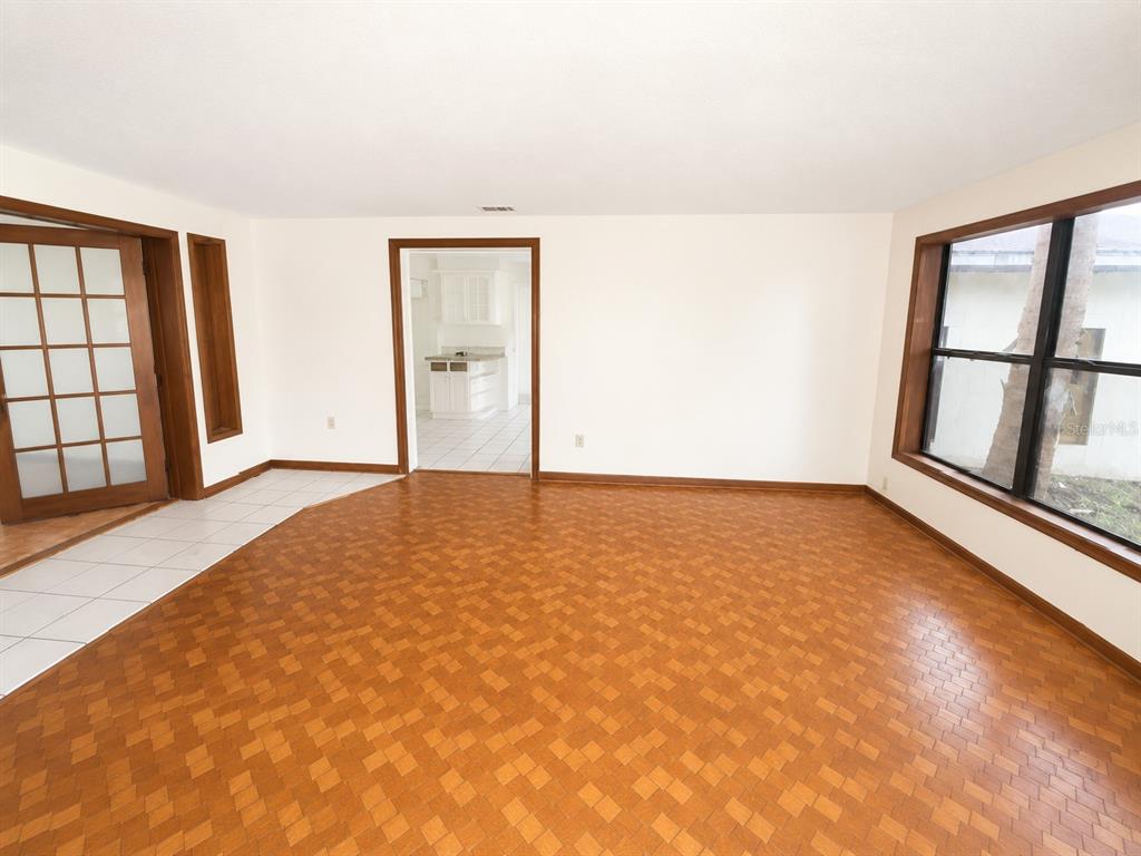 An empty room with parquet flooring, a large window, and a doorway leading to a kitchen — 217 PLUMOSA ROAD, DEBARY, FL