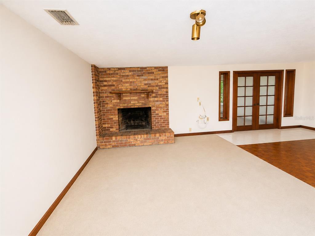 A living room features a brick fireplace, beige carpeting, and French doors leading outside — 217 PLUMOSA ROAD, DEBARY, FL