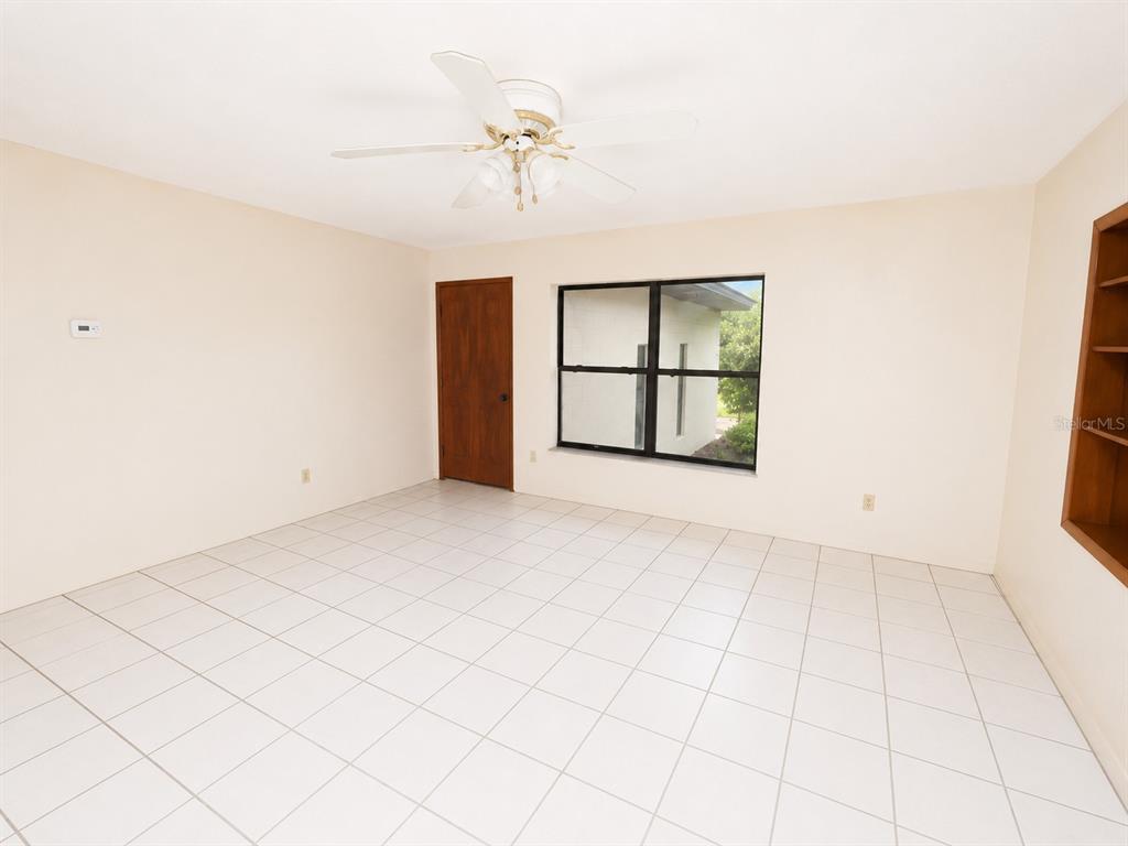 An empty room features white tile flooring, a ceiling fan, a window, and a wooden door — 217 PLUMOSA ROAD, DEBARY, FL