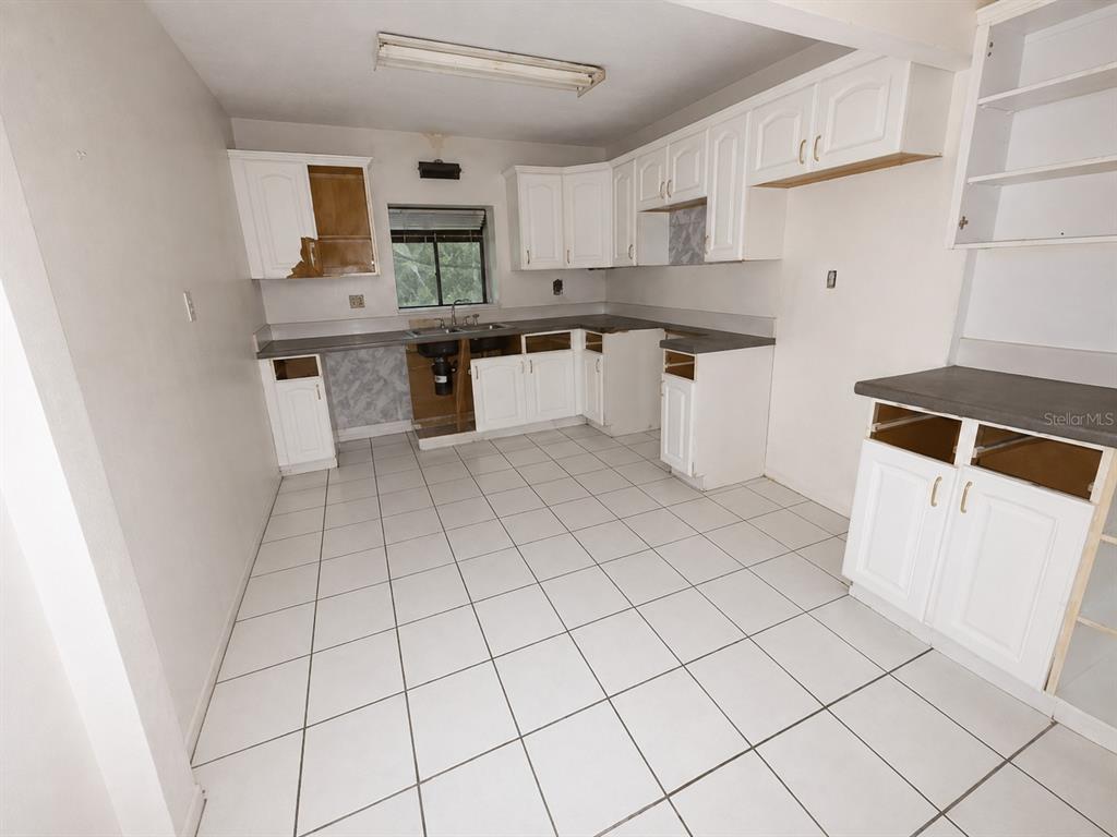 An unfinished kitchen features white cabinets, gray countertops, and white tile flooring — 217 PLUMOSA ROAD, DEBARY, FL