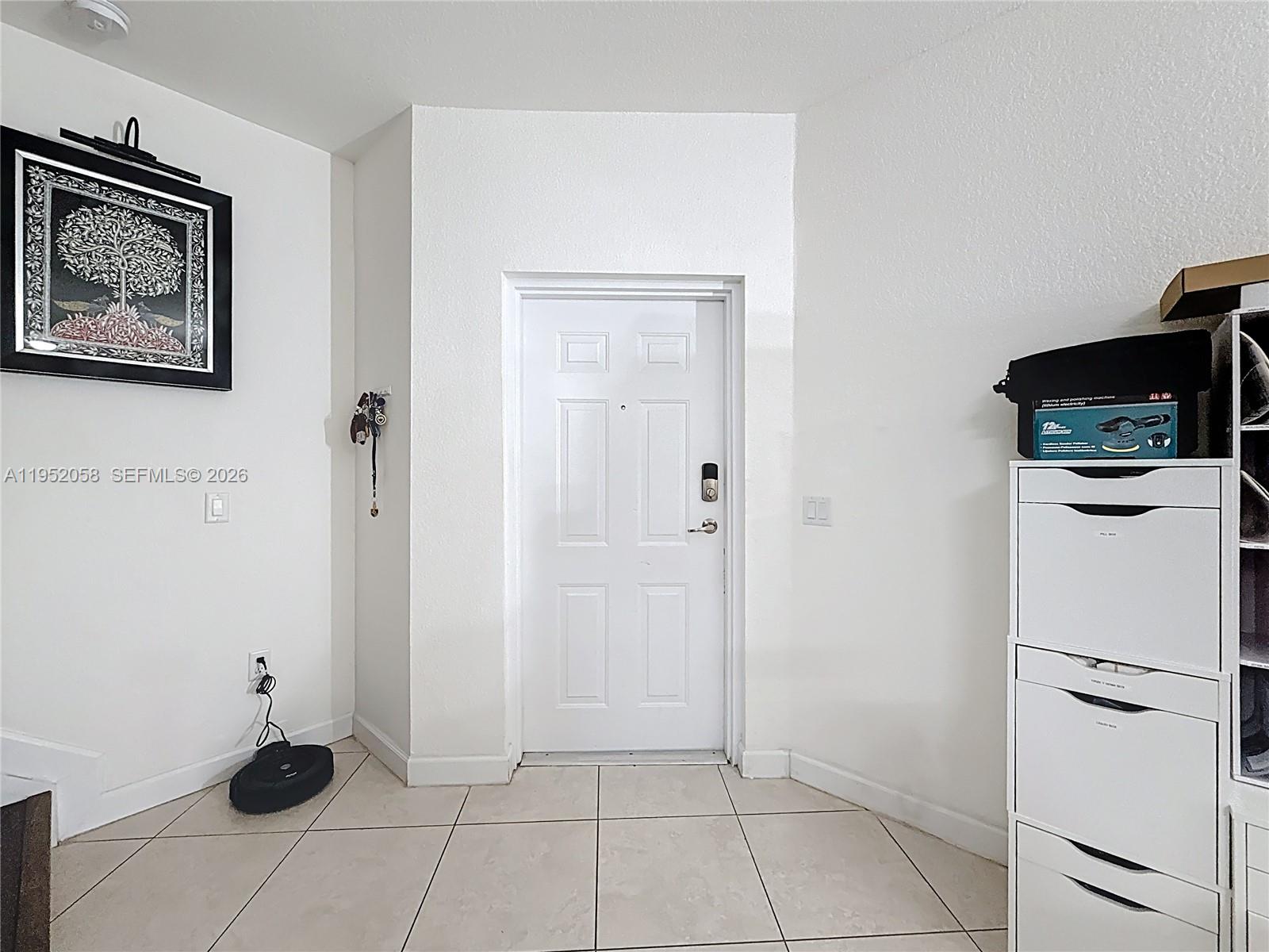 An entryway features a white door, tiled flooring, a framed wall art piece, and storage drawers — 260 NW 109th Ave # 206, Miami FL 33172, MIAMI, FL