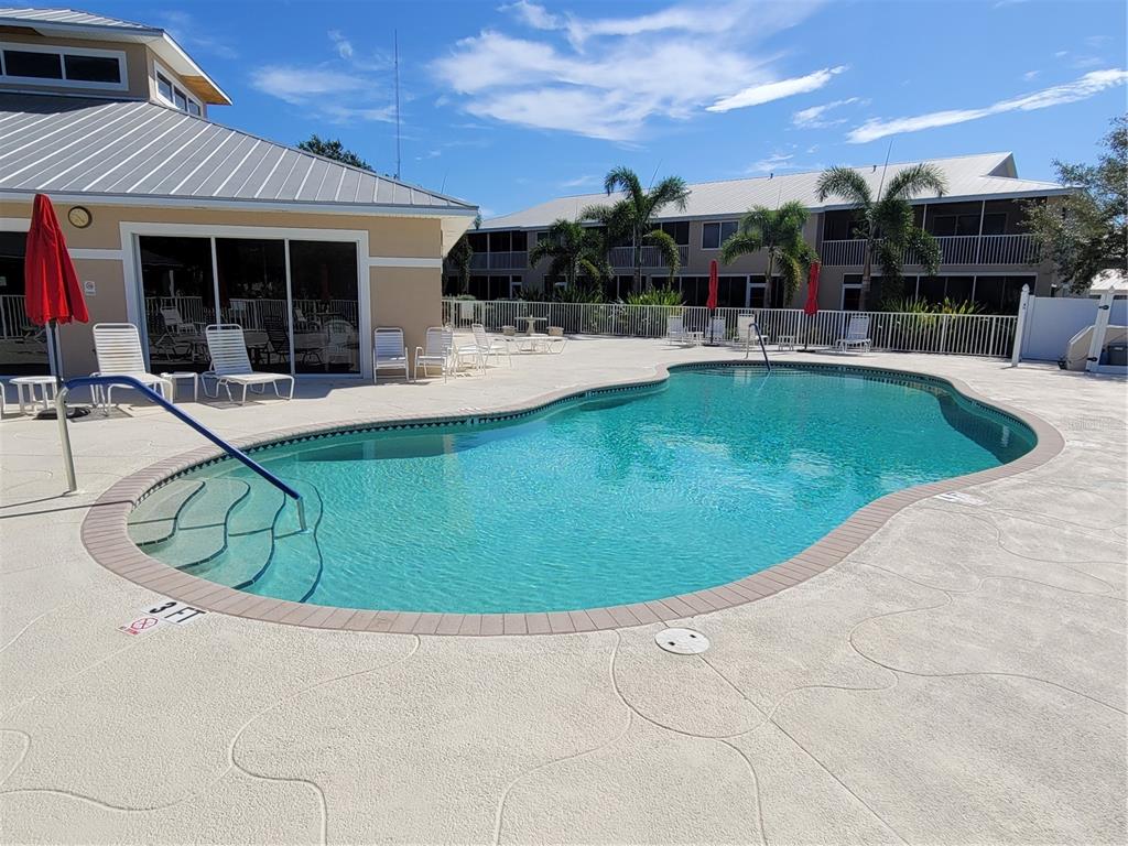 An outdoor swimming pool with a shallow entry area sits beside a building and patio — 9550 FIDDLERS GREEN CIRCLE UNIT 105, ROTONDA WEST, FL