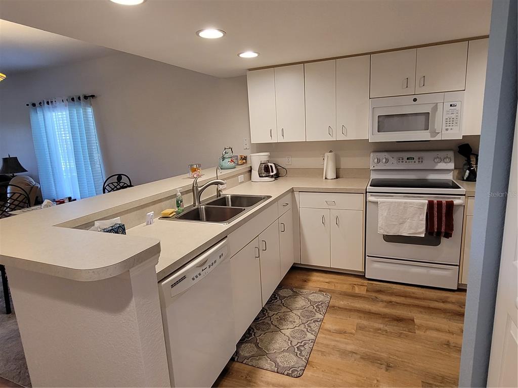 A kitchen features white cabinets, laminate countertops, a double sink, and a white appliance suite — 9550 FIDDLERS GREEN CIRCLE UNIT 105, ROTONDA WEST, FL