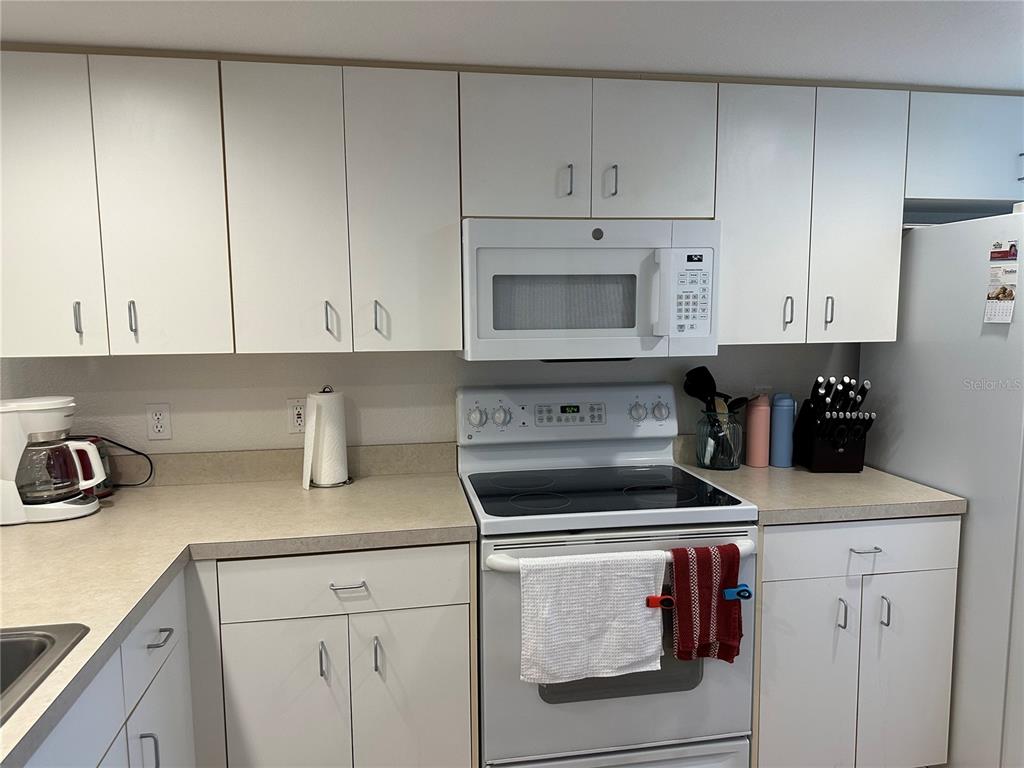 A kitchen features white cabinets, a white stove, a microwave, and light-colored countertops — 9550 FIDDLERS GREEN CIRCLE UNIT 105, ROTONDA WEST, FL