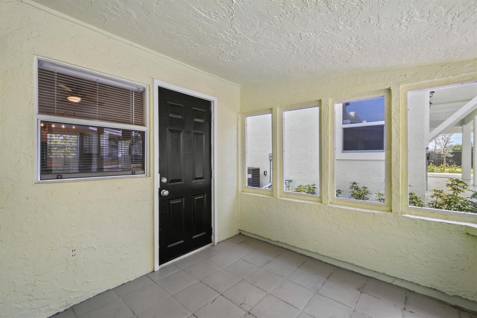 A sunroom with yellow textured walls, a black door, and gray tiled flooring — 627 Bunker Road, West Palm Beach FL 33405, WEST PALM BEACH, FL