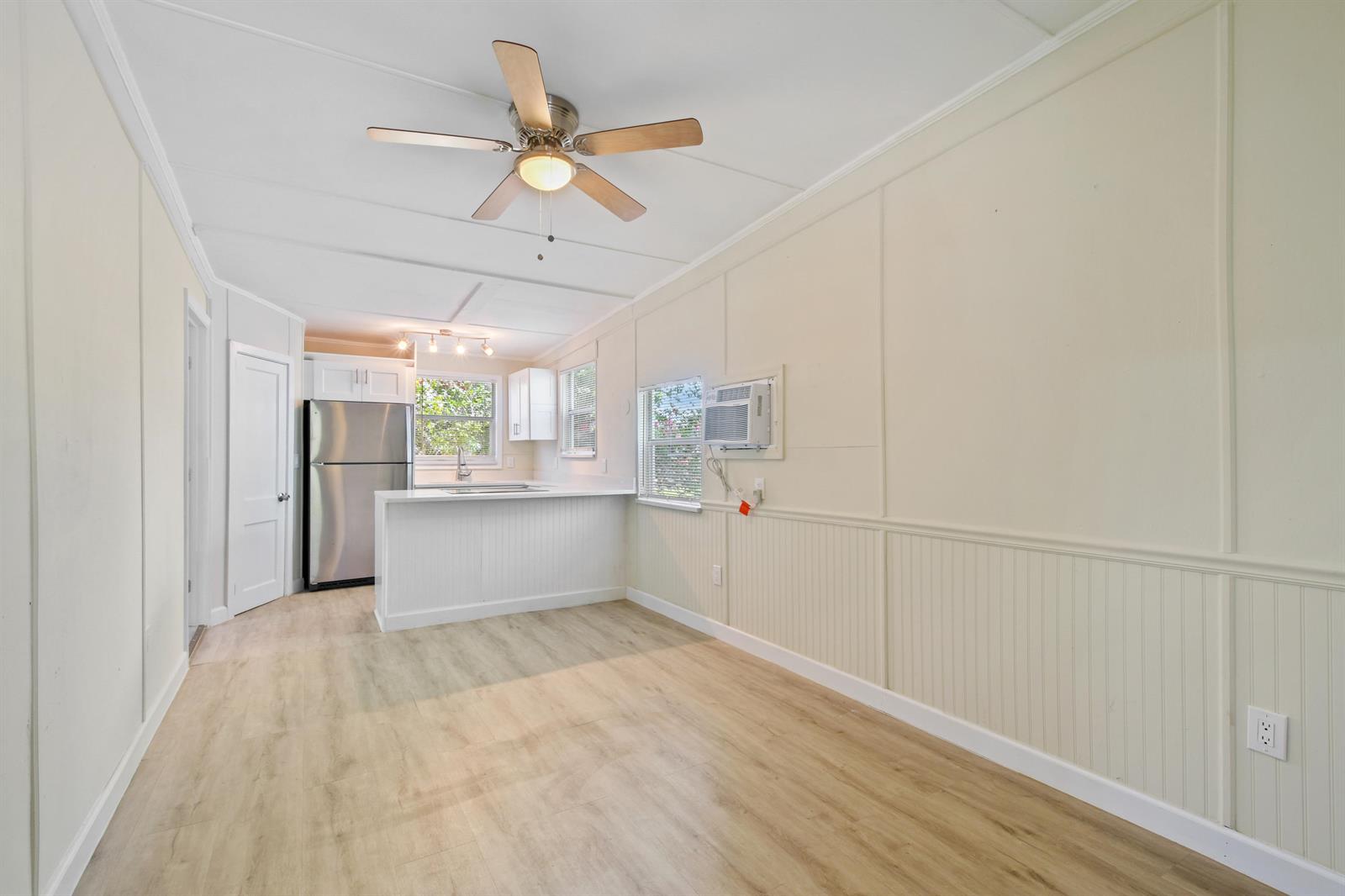 A kitchen and living area with light wood floors, white wainscoting, and a ceiling fan — 627 Bunker Road, West Palm Beach FL 33405, WEST PALM BEACH, FL