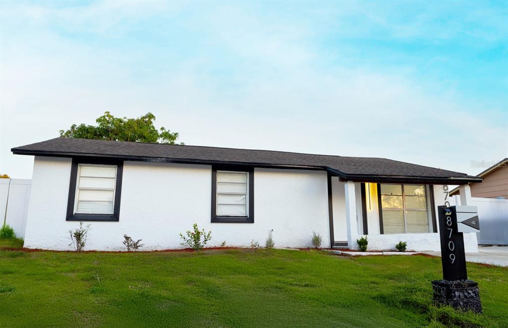 A single-story white house with black trim and a dark shingled roof sits on grass — 8709 MARLIN COURT, TAMPA, FL