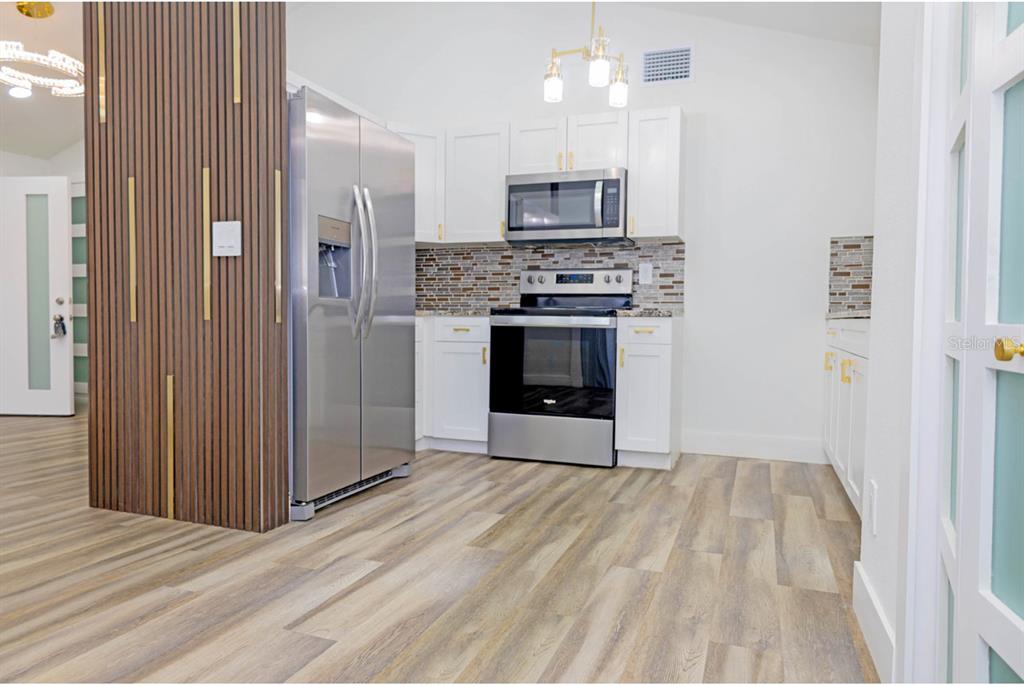 A kitchen features white cabinets, stainless steel appliances, a tiled backsplash, and wood-look flooring — 8709 MARLIN COURT, TAMPA, FL