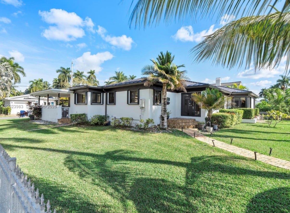 A single-story white house with a dark roof and trim sits on a grassy lawn — HOLLYWOOD, FL