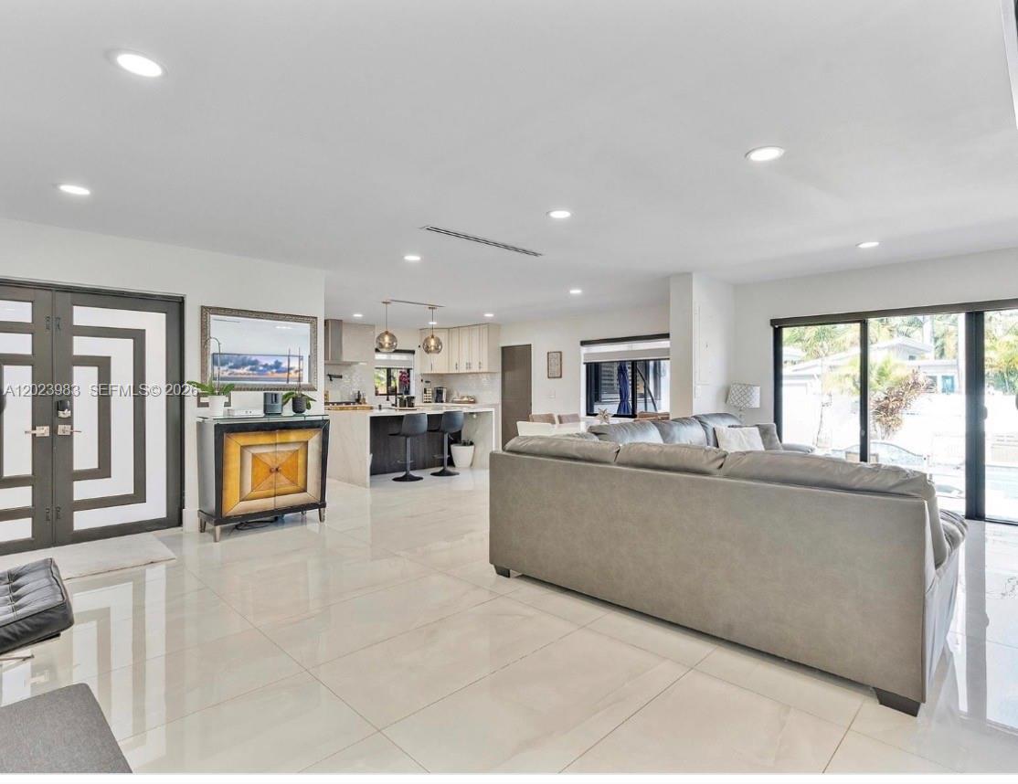 A modern open-concept living room and kitchen feature white tile floors and a gray sofa — HOLLYWOOD, FL