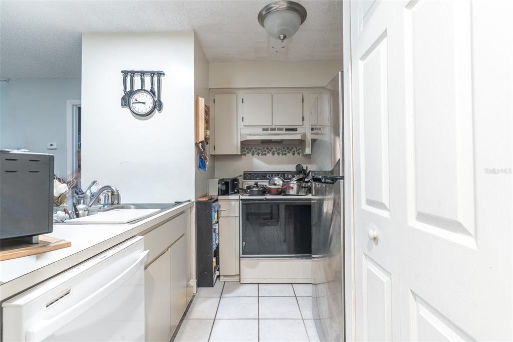 A galley-style kitchen features white cabinets, tile flooring, and stainless steel appliances — 6085 TOPHER TRAIL UNIT 6085, MULBERRY, FL