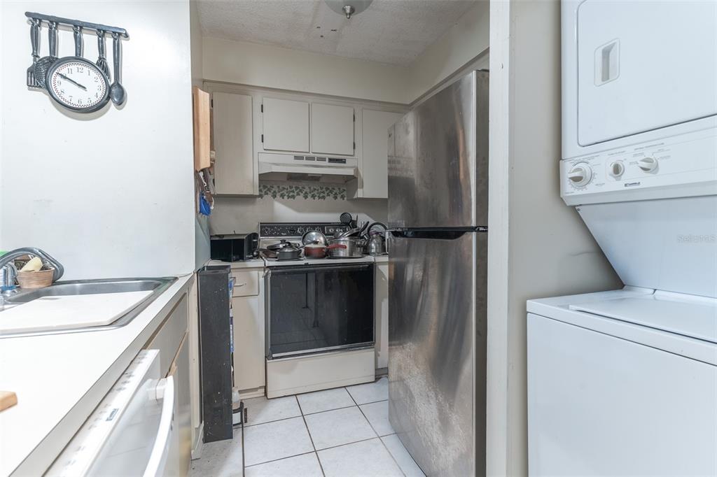 A small kitchen features white cabinets, a stainless steel refrigerator, and a stacked laundry unit — 6085 TOPHER TRAIL UNIT 6085, MULBERRY, FL