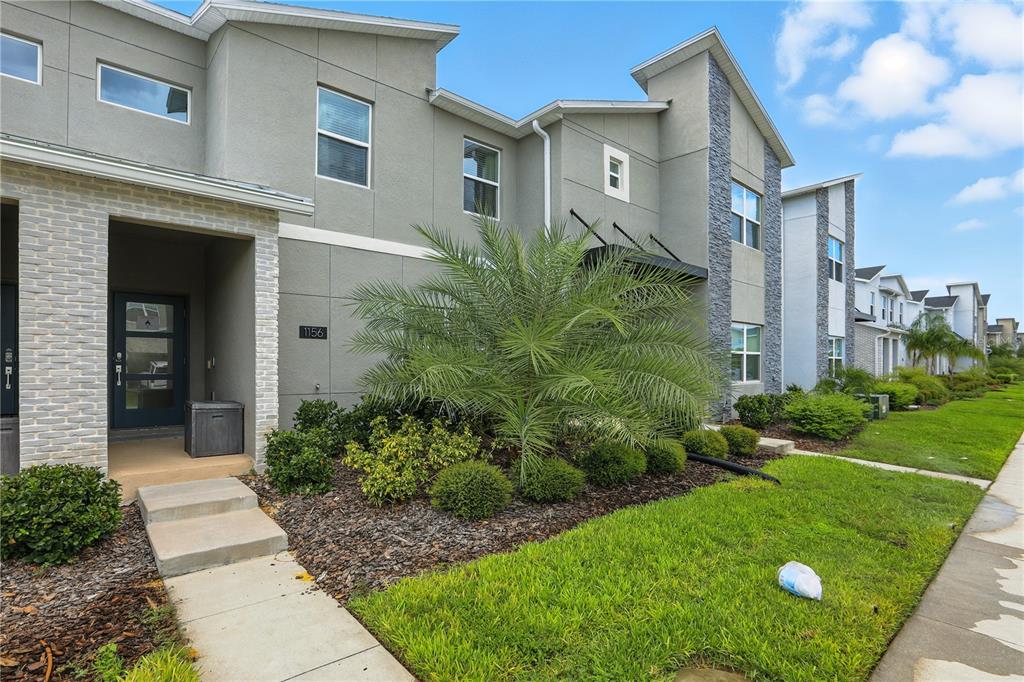 A two-story townhouse exterior features gray stucco, stone accents, a palm tree, and a walkway — 1156 KINGSBARN STREET, DAVENPORT, FL