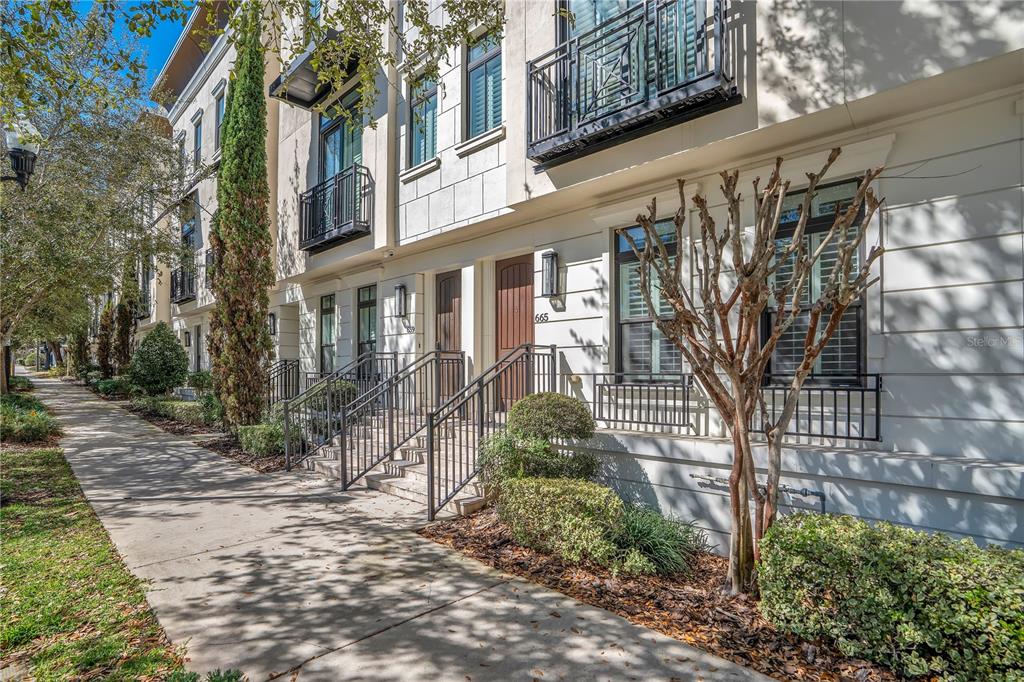 A row of three-story townhomes with white facades, balconies, and mature trees in front — 665 JACKSON STREET, ORLANDO, FL