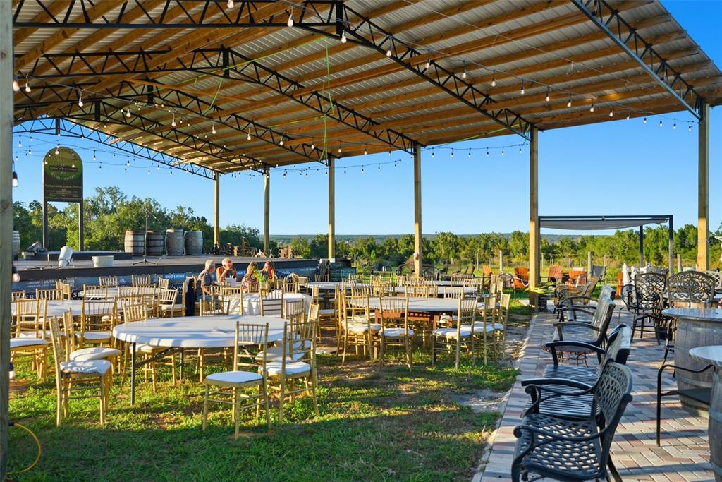 An outdoor covered event space features round tables with gold chairs and a stage area — 21509 SNOW HILL ROAD, BROOKSVILLE, FL