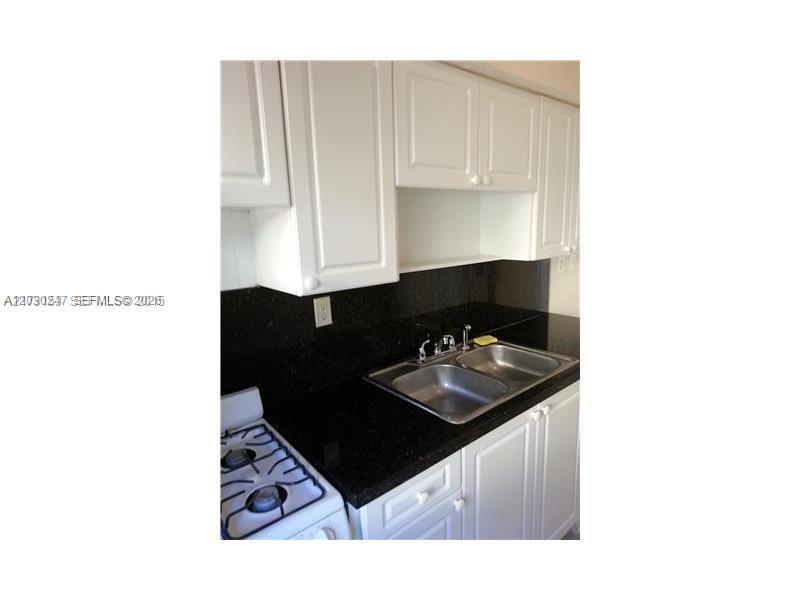 A kitchen features white cabinets, black countertops, a double sink, and a white gas stove — 8320 Crespi Blvd # 11, Miami Beach FL 33141, MIAMI BEACH, FL
