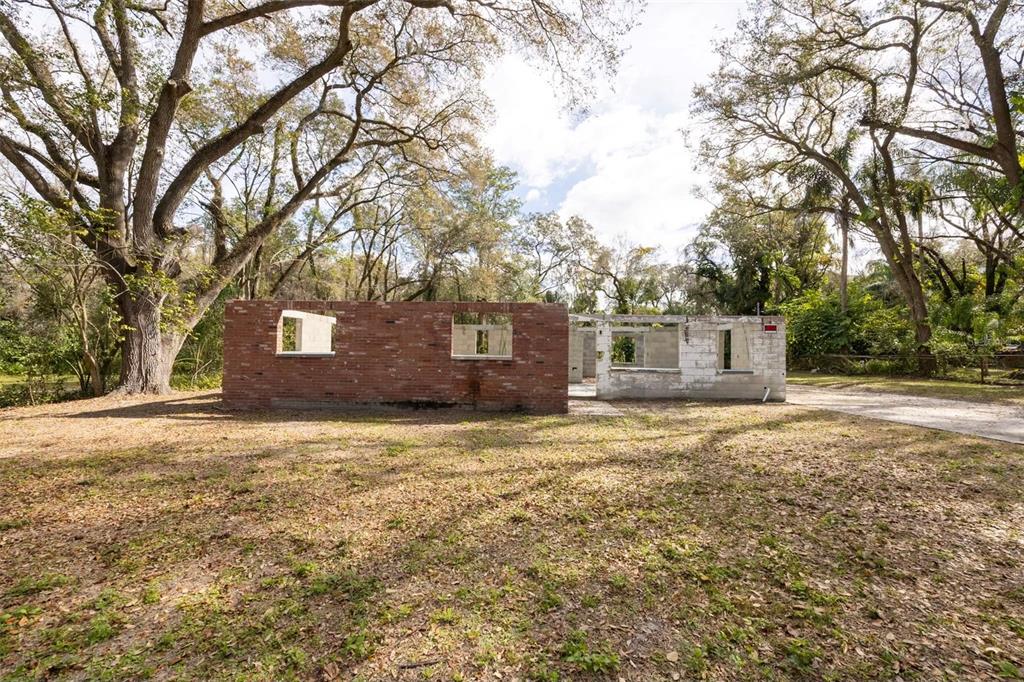 A partially demolished brick and concrete block structure stands on a wooded, grassy lot — 5515 N FALKENBURG ROAD, TAMPA, FL