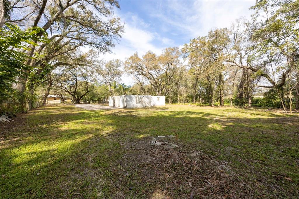 A grassy lot features a small, unfinished concrete structure surrounded by mature trees — 5515 N FALKENBURG ROAD, TAMPA, FL