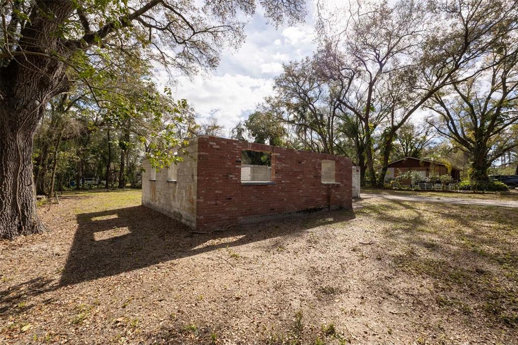 An exterior view of a brick building shell with open window frames on a wooded lot — 5515 N FALKENBURG ROAD, TAMPA, FL