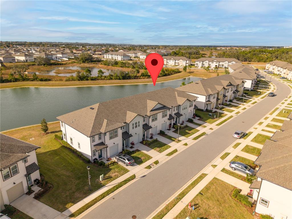 An aerial view shows a row of townhomes situated along a pond in a neighborhood — 710 LONGBOAT DRIVE, DAVENPORT, FL