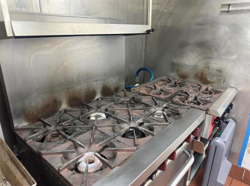 A commercial gas range with multiple burners sits in front of a stainless steel backsplash — 517 N SEMORAN BOULEVARD, ORLANDO, FL