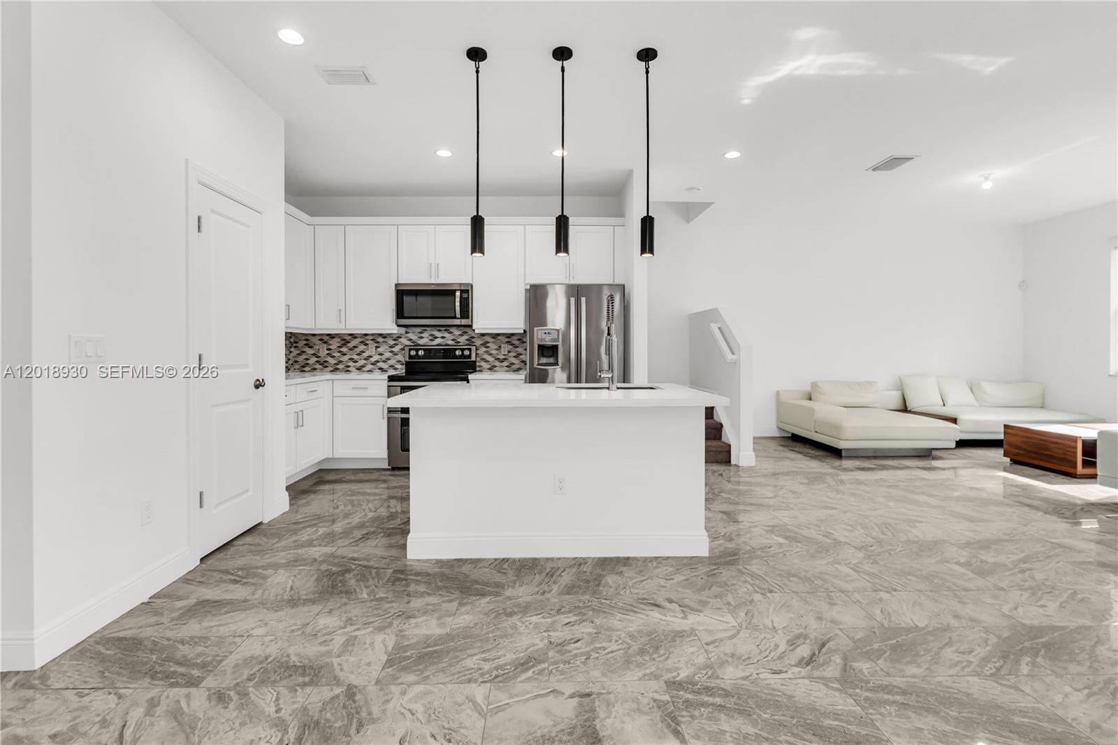A modern kitchen with white cabinets, a central island, and gray marble-patterned tile flooring — 582 Parsons Way, Deerfield Beach FL 33442, DEERFIELD BEACH, FL