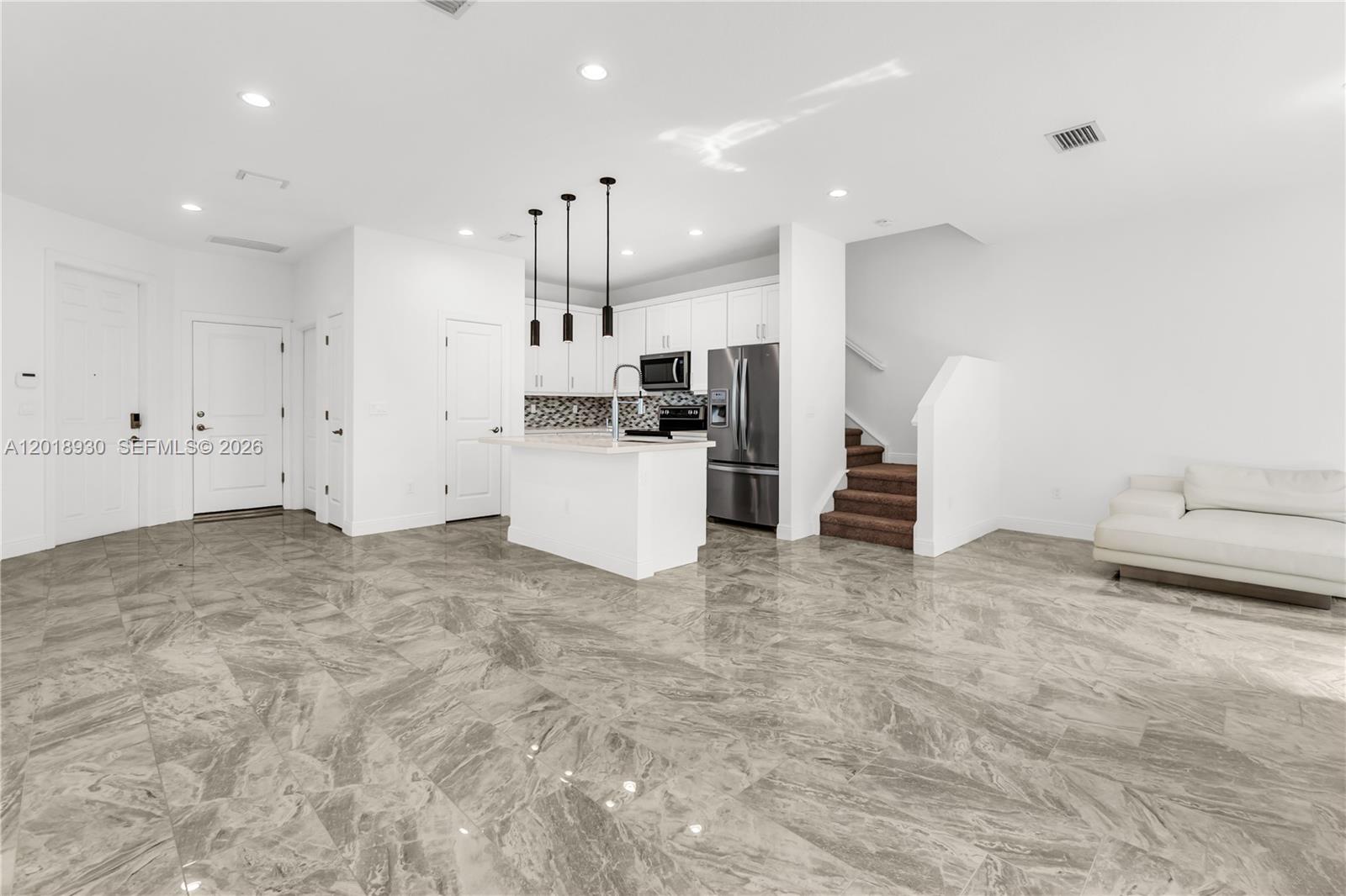 An open-concept kitchen with white cabinets and a marble-tiled floor overlooks a living area — 582 Parsons Way, Deerfield Beach FL 33442, DEERFIELD BEACH, FL