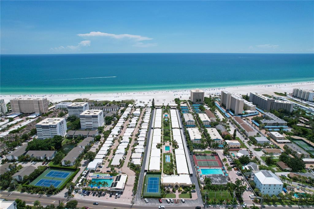 An aerial view shows a beachfront resort complex with multiple buildings, swimming pools, and tennis courts — 6006 MIDNIGHT PASS ROAD UNIT 16, SARASOTA, FL