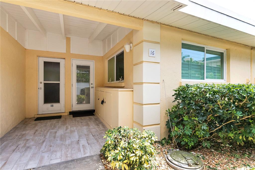The exterior of a yellow building features two white doors, a window, and landscaping — 6006 MIDNIGHT PASS ROAD UNIT 16, SARASOTA, FL