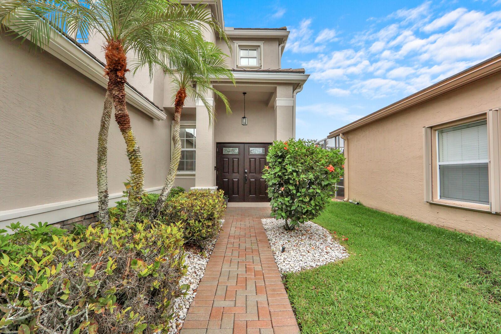 A brick walkway leads to the dark double front doors of a beige two-story house — 5690 Saddle Trail Lane, Lake Worth FL 33449, LAKE WORTH, FL