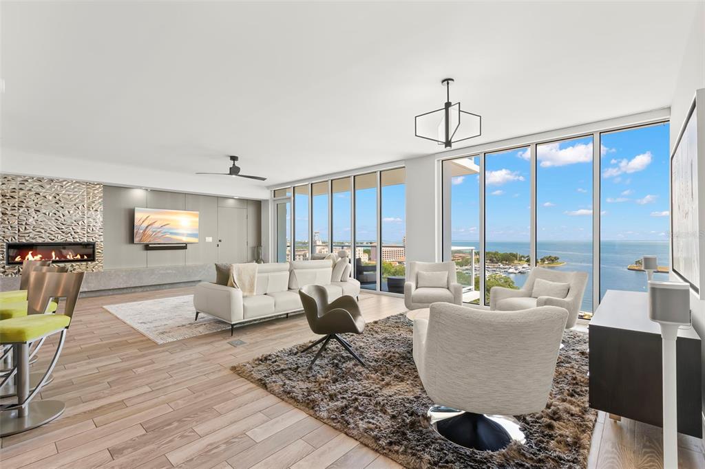 A modern living room features a fireplace, white sofa, armchairs, and floor-to-ceiling windows overlooking water — 176 4TH AVENUE NE UNIT 1102, ST PETERSBURG, FL