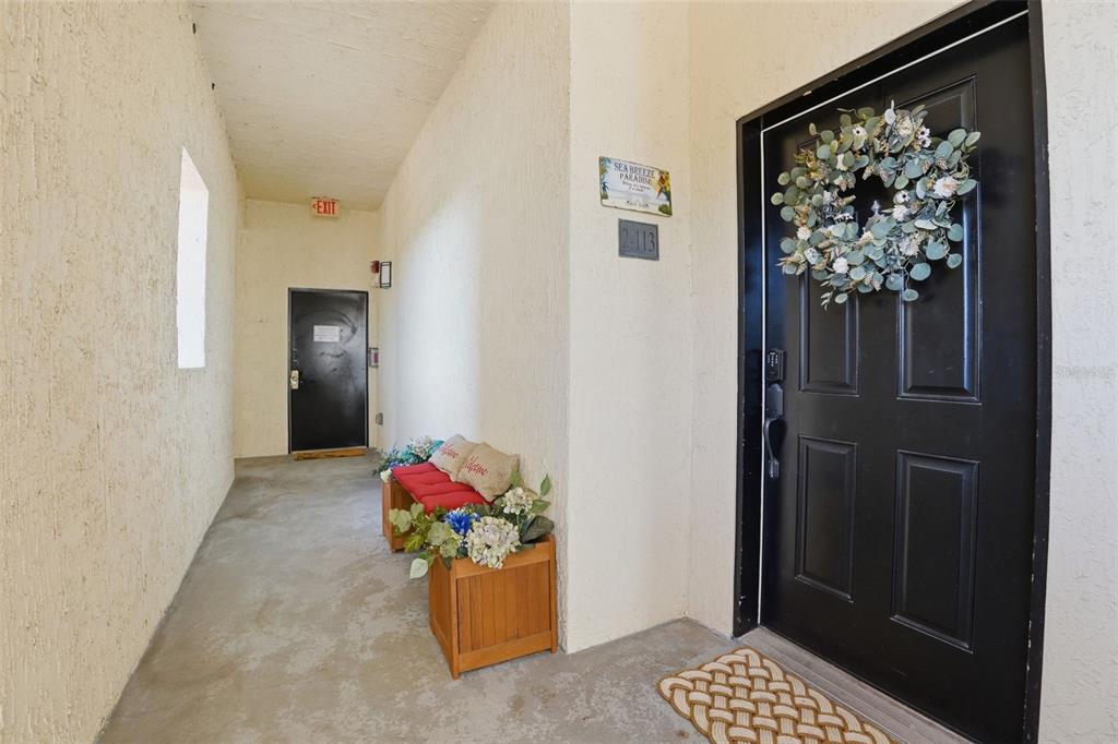 A black front door with a wreath sits in a concrete hallway with a bench — 200 BELLA HARBOR COURT UNIT 113, PALM COAST, FL
