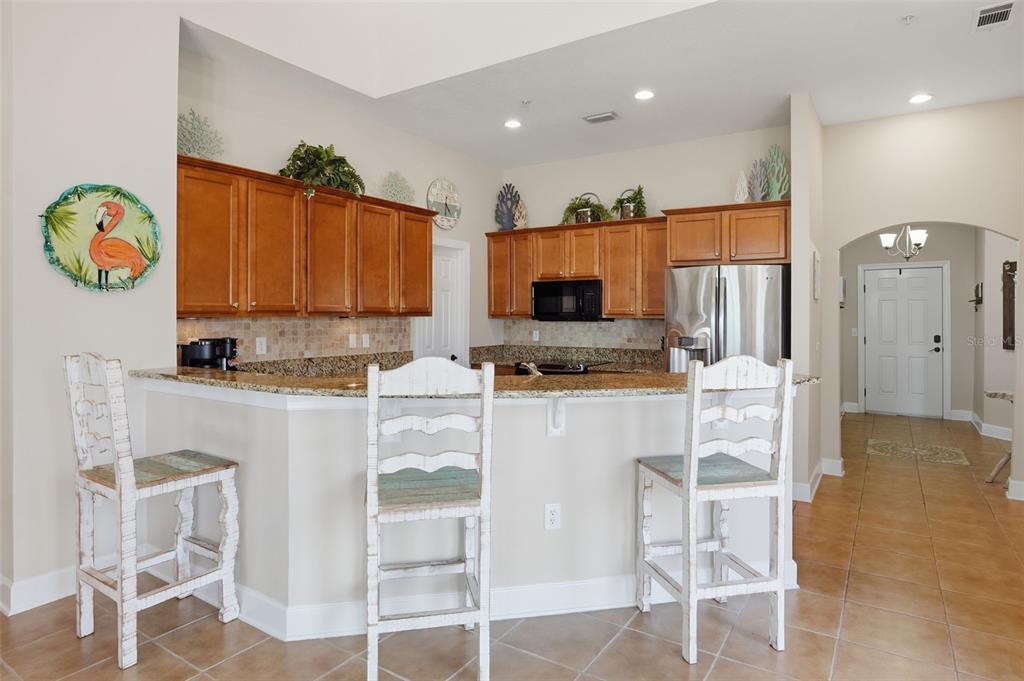 A kitchen features wood cabinets, granite countertops, a breakfast bar with three chairs, and tile flooring — 200 BELLA HARBOR COURT UNIT 113, PALM COAST, FL