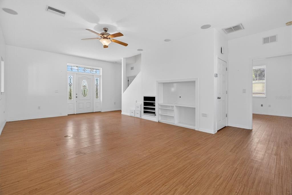 A bright living room features white walls, wood-look flooring, a ceiling fan, and built-in shelving — 38327 HAMRICH DRIVE, DADE CITY, FL