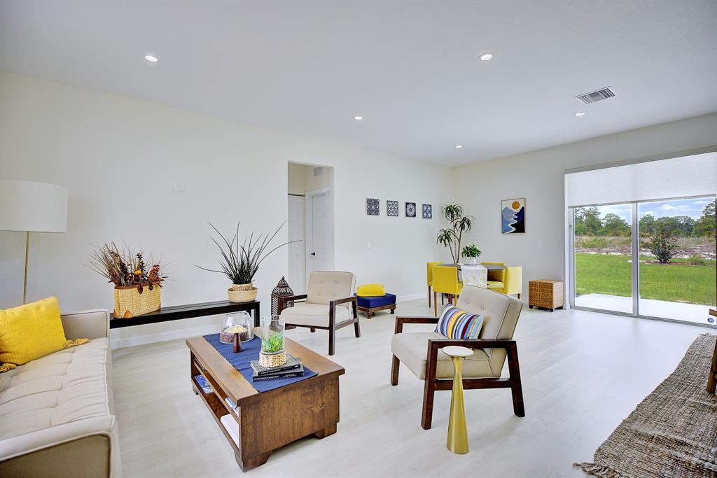 A bright living and dining area with light wood floors, yellow accents, and sliding doors — 109 FIRE ISLAND AVENUE NE, LAKE PLACID, FL