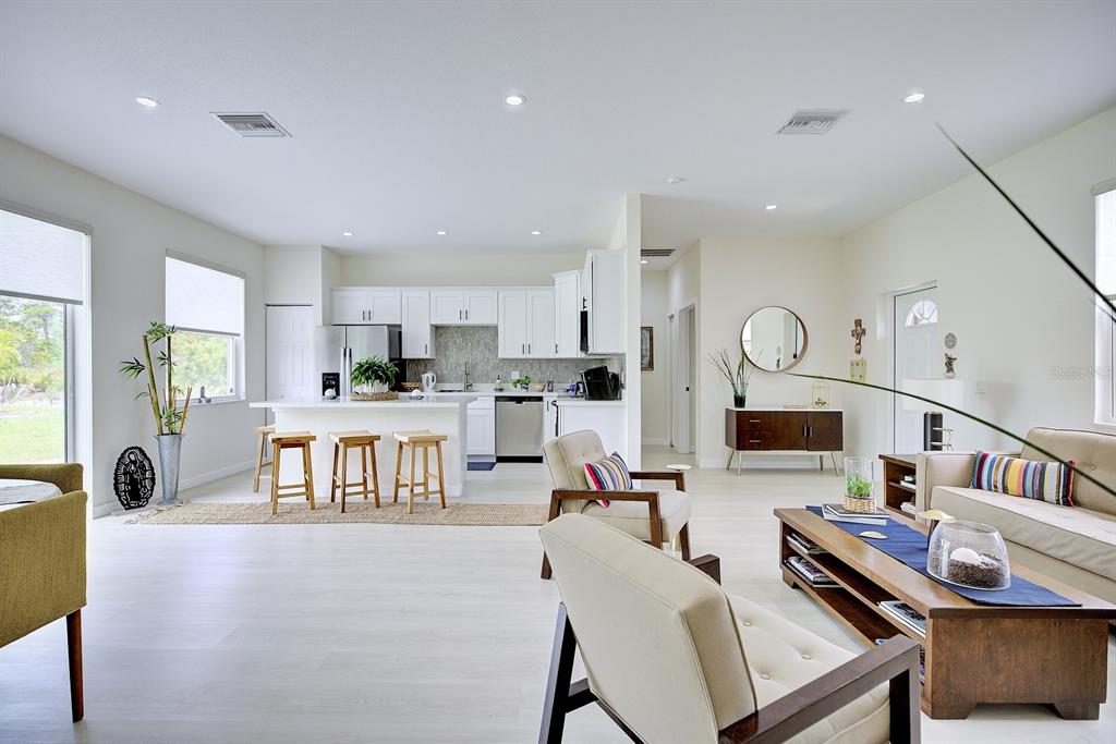 An open-concept living room and kitchen featuring white cabinetry, light wood flooring, and modern furniture — 109 FIRE ISLAND AVENUE NE, LAKE PLACID, FL