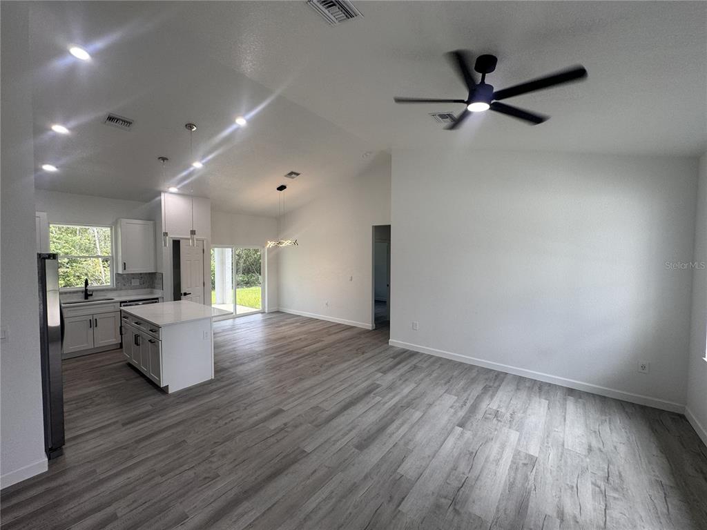 An open-concept kitchen and living area features white cabinetry, a center island, and wood-look flooring — 7624 ANCHA STREET, SEBRING, FL