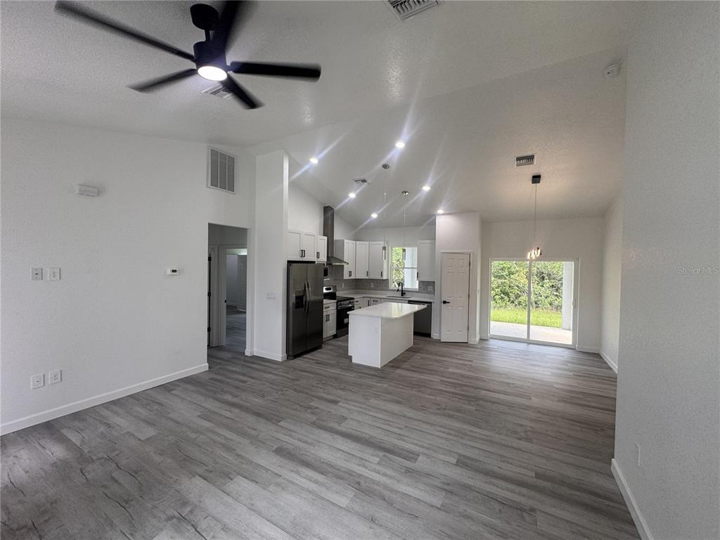 An open-concept kitchen and living area features white cabinetry, a center island, and wood-look flooring — 7624 ANCHA STREET, SEBRING, FL